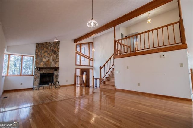 unfurnished living room featuring hardwood / wood-style floors, a stone fireplace, beamed ceiling, and an inviting chandelier