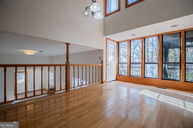 empty room featuring a towering ceiling, wood-type flooring, a textured ceiling, and a notable chandelier