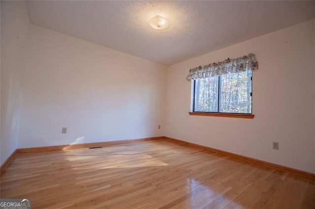 spare room with vaulted ceiling, hardwood / wood-style floors, and a textured ceiling