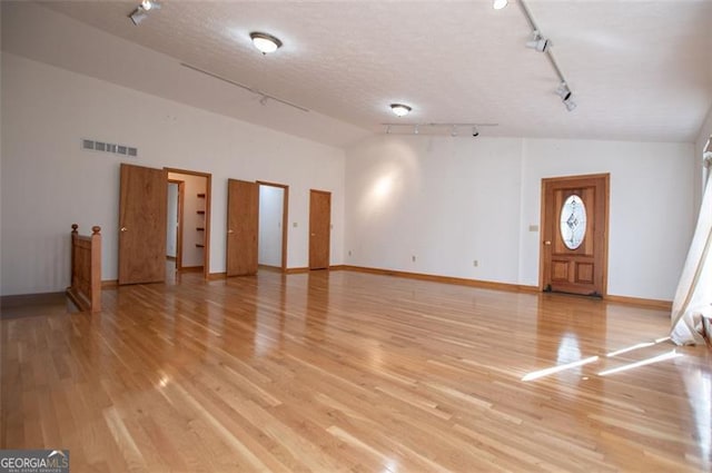 interior space featuring a textured ceiling, light hardwood / wood-style floors, rail lighting, and high vaulted ceiling