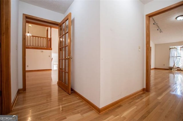 hall featuring track lighting, a textured ceiling, and light hardwood / wood-style flooring