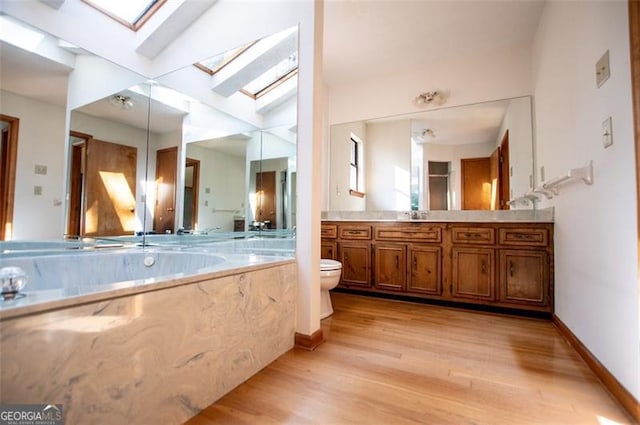 bathroom with vaulted ceiling with skylight, vanity, wood-type flooring, and toilet