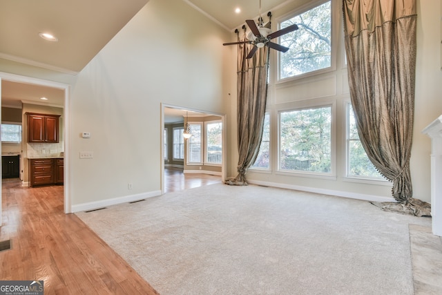 unfurnished living room with ceiling fan, light wood-type flooring, ornamental molding, and high vaulted ceiling