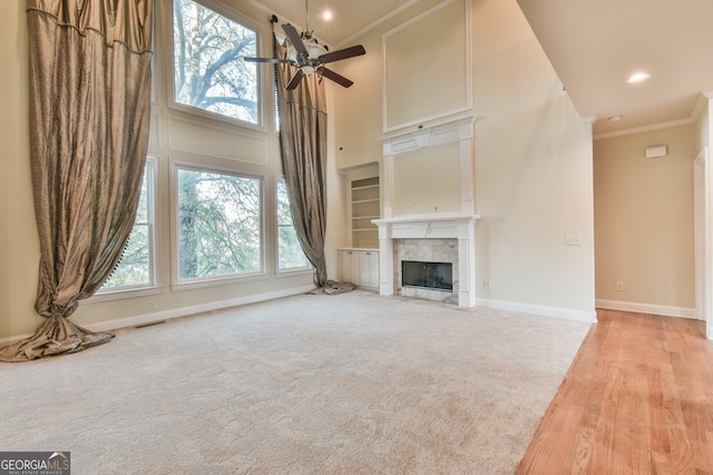 unfurnished living room featuring a tile fireplace, ceiling fan, light hardwood / wood-style flooring, crown molding, and a towering ceiling