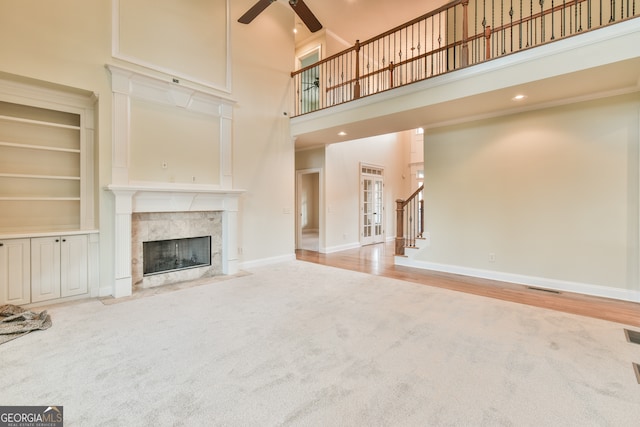 unfurnished living room with a fireplace, a towering ceiling, light hardwood / wood-style floors, and ceiling fan