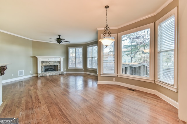 unfurnished living room featuring ceiling fan, light hardwood / wood-style floors, a stone fireplace, and crown molding