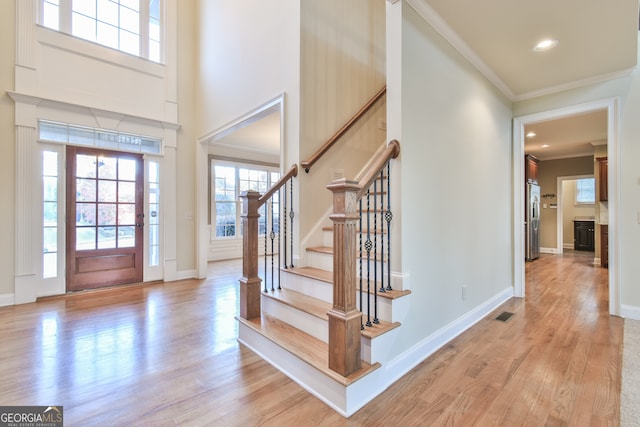 foyer entrance with a towering ceiling, ornamental molding, and light wood-type flooring