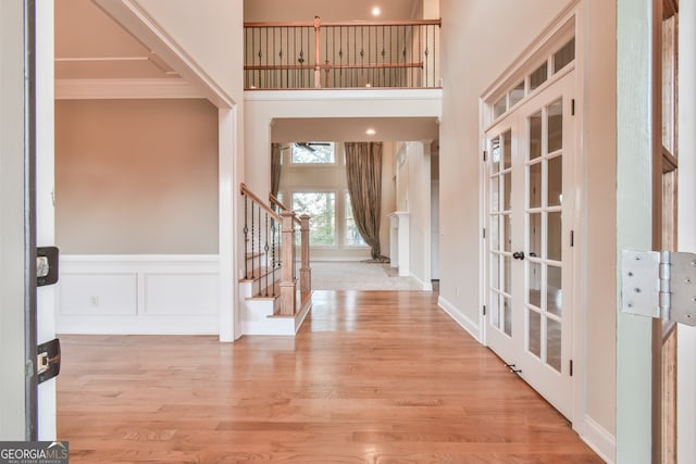 entrance foyer featuring crown molding, french doors, a towering ceiling, and light hardwood / wood-style floors