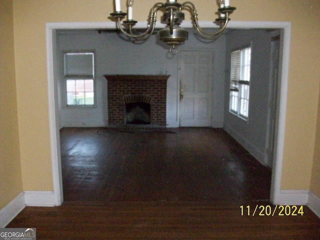 unfurnished living room featuring dark wood-type flooring, a chandelier, and a brick fireplace