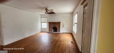 unfurnished living room with ceiling fan, dark hardwood / wood-style flooring, and a brick fireplace