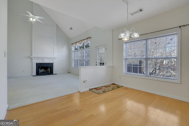 unfurnished living room with vaulted ceiling, wood-type flooring, ceiling fan with notable chandelier, and a fireplace