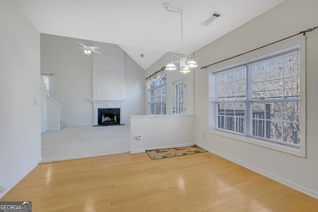 unfurnished dining area with a fireplace, ceiling fan with notable chandelier, vaulted ceiling, and a healthy amount of sunlight