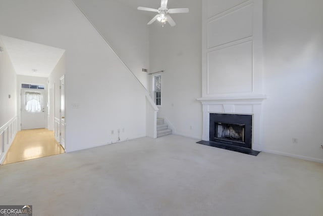 unfurnished living room featuring a high ceiling, a large fireplace, light carpet, and ceiling fan