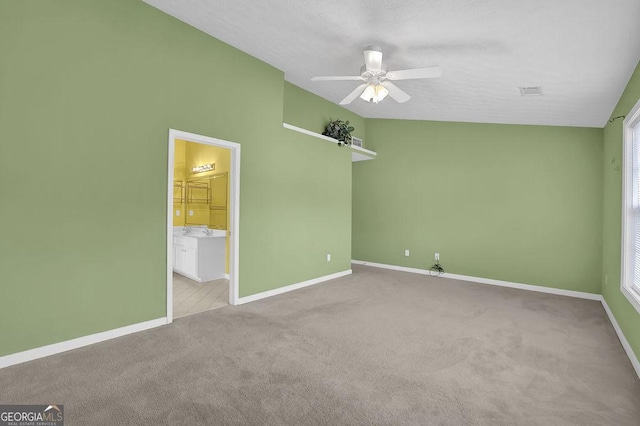 unfurnished bedroom featuring light carpet, connected bathroom, vaulted ceiling, and ceiling fan