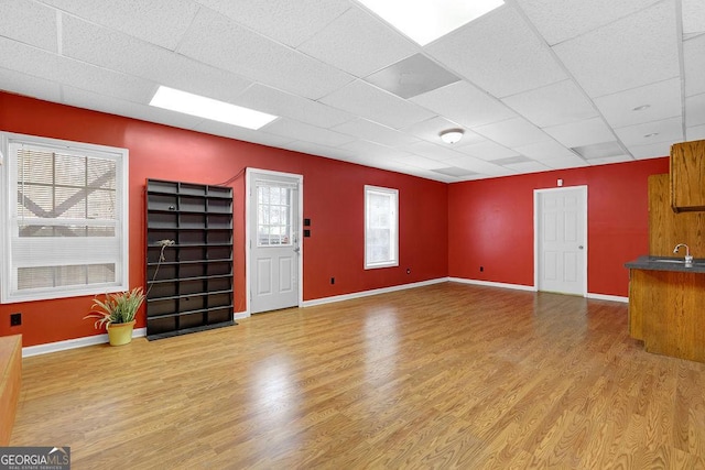 unfurnished living room with a paneled ceiling, plenty of natural light, sink, and light hardwood / wood-style flooring