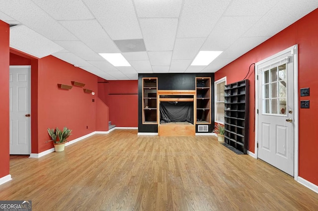 unfurnished living room featuring wood-type flooring, built in features, and a drop ceiling