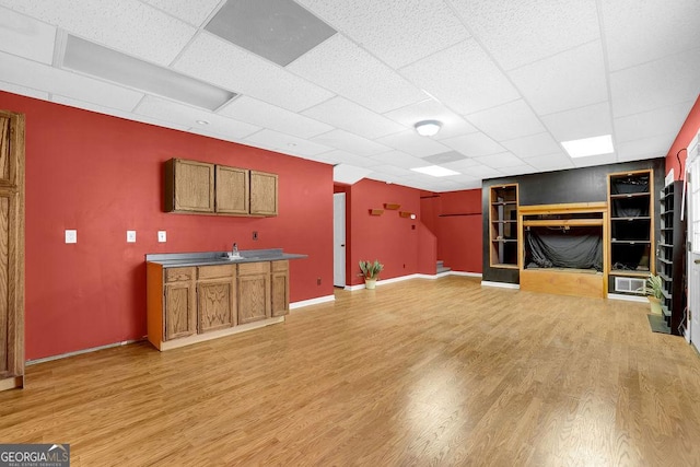 unfurnished living room with built in shelves, light hardwood / wood-style floors, and a drop ceiling