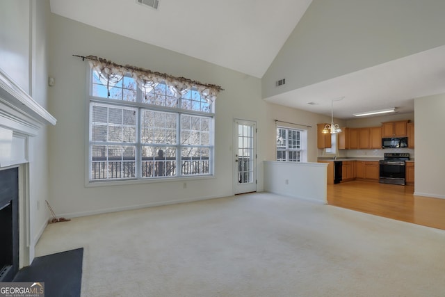 unfurnished living room with an inviting chandelier, high vaulted ceiling, and light carpet