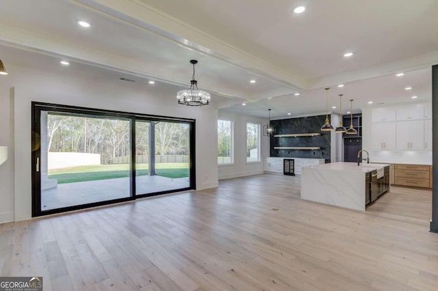 unfurnished living room with beamed ceiling, light wood-type flooring, a notable chandelier, and sink