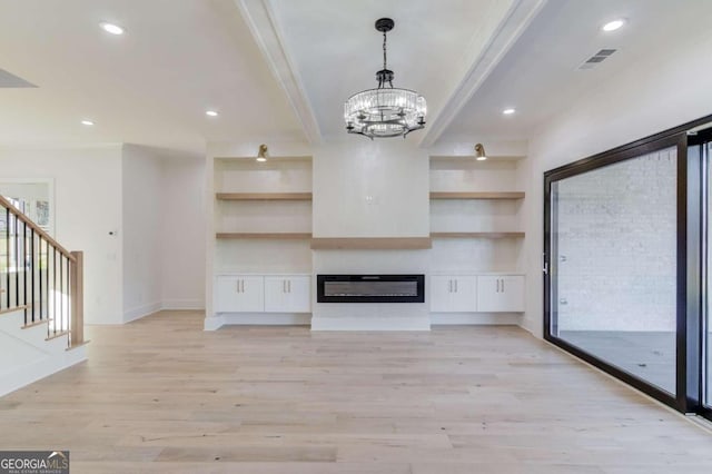 unfurnished living room featuring built in shelves, ornamental molding, a notable chandelier, and light wood-type flooring