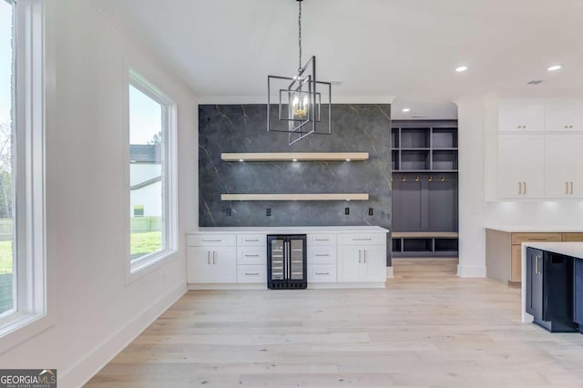 bar with light wood-type flooring, beverage cooler, white cabinets, a chandelier, and hanging light fixtures