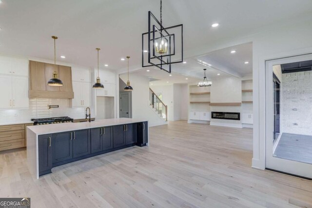 kitchen featuring a large island with sink, light hardwood / wood-style floors, white cabinetry, and hanging light fixtures