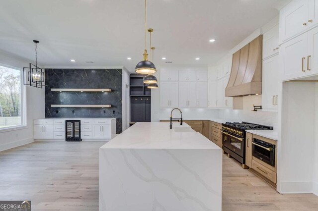 kitchen with decorative light fixtures, white cabinets, an island with sink, and range with two ovens