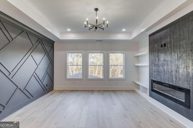 unfurnished living room featuring a tray ceiling, light hardwood / wood-style flooring, a notable chandelier, and ornamental molding