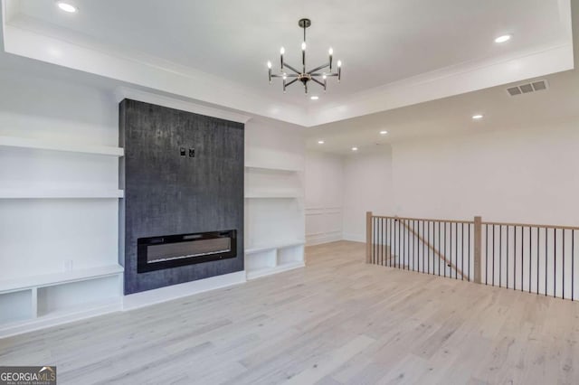 unfurnished living room featuring built in shelves, light hardwood / wood-style floors, a fireplace, and an inviting chandelier