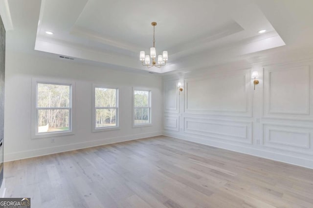 empty room featuring a chandelier, light hardwood / wood-style floors, and a tray ceiling