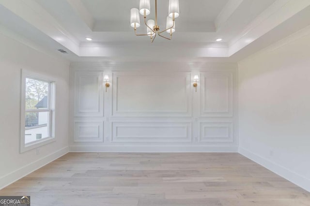 spare room with a chandelier, light hardwood / wood-style flooring, a raised ceiling, and crown molding