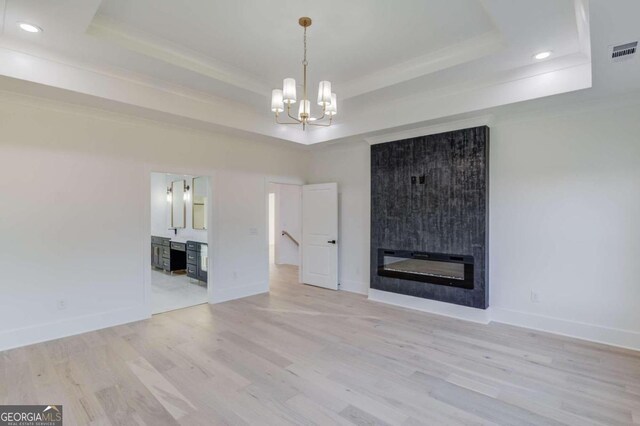 unfurnished living room with a raised ceiling, a large fireplace, light hardwood / wood-style flooring, and a chandelier