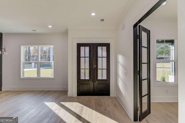 foyer entrance with light hardwood / wood-style floors, ornamental molding, and french doors