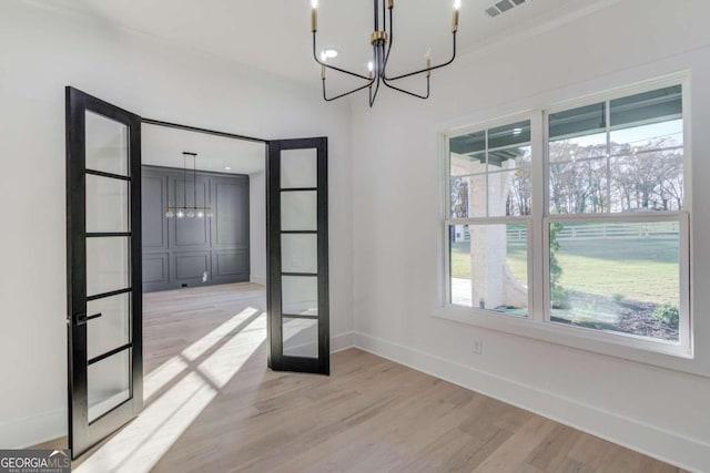 unfurnished room featuring a chandelier, french doors, light wood-type flooring, and ornamental molding