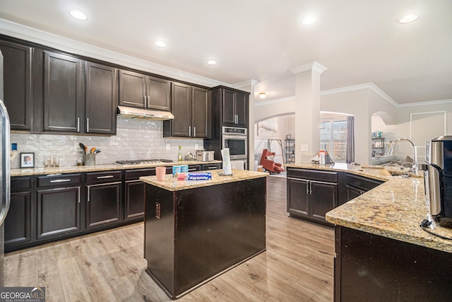 kitchen with crown molding, light hardwood / wood-style flooring, a kitchen island, and light stone countertops