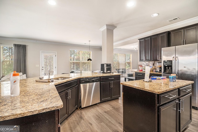 kitchen with pendant lighting, stainless steel appliances, plenty of natural light, and a center island with sink