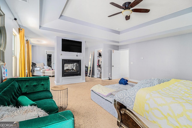 bedroom with a multi sided fireplace, carpet flooring, ceiling fan, a tray ceiling, and a closet