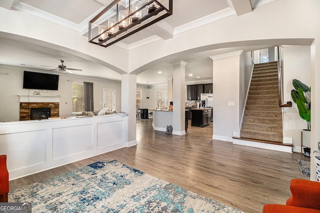 living room featuring ceiling fan, a stone fireplace, dark hardwood / wood-style flooring, and crown molding