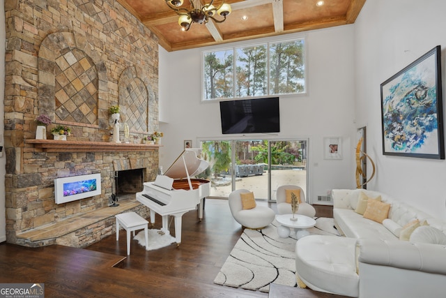 living room featuring dark wood-type flooring, coffered ceiling, a stone fireplace, a notable chandelier, and a towering ceiling