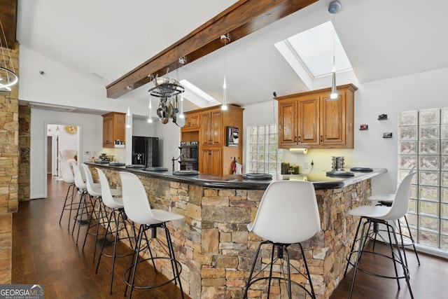 kitchen with kitchen peninsula, black appliances, beamed ceiling, dark hardwood / wood-style floors, and a breakfast bar area