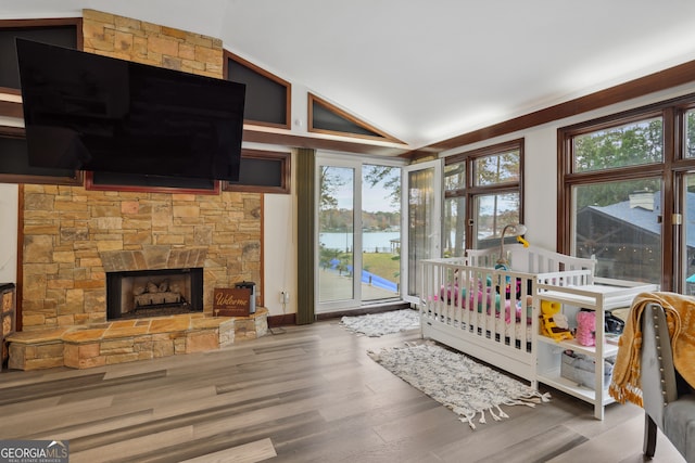 bedroom featuring high vaulted ceiling, a stone fireplace, wood-type flooring, and a water view