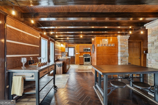 kitchen with wood walls, parquet floors, sink, appliances with stainless steel finishes, and beam ceiling