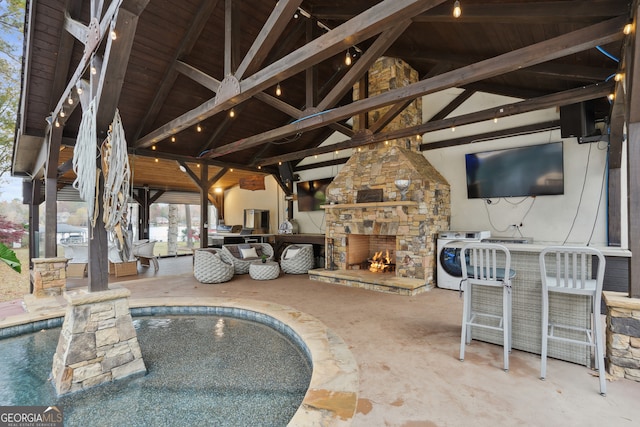 view of patio / terrace featuring washer / clothes dryer, a bar, and an outdoor stone fireplace