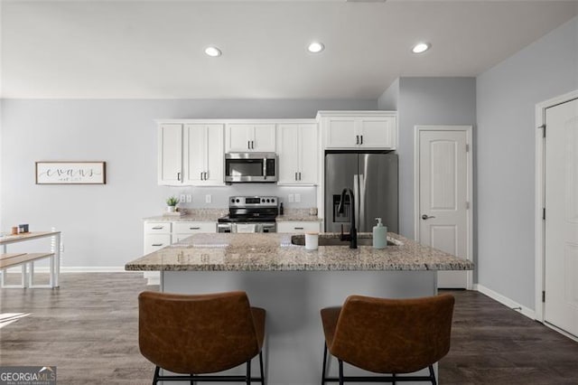 kitchen featuring white cabinetry, dark wood-type flooring, a kitchen breakfast bar, an island with sink, and appliances with stainless steel finishes