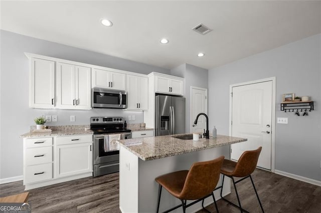 kitchen with light stone countertops, appliances with stainless steel finishes, sink, a center island with sink, and white cabinetry