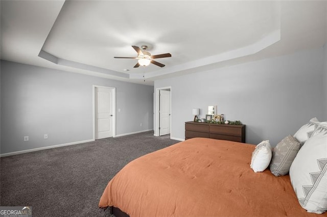 bedroom featuring ceiling fan, dark carpet, and a tray ceiling