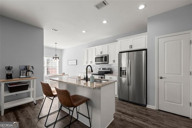 kitchen with a kitchen bar, appliances with stainless steel finishes, dark hardwood / wood-style flooring, a kitchen island with sink, and white cabinets