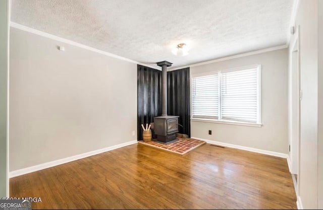 unfurnished living room featuring wood-type flooring, a textured ceiling, a wood stove, and ornamental molding