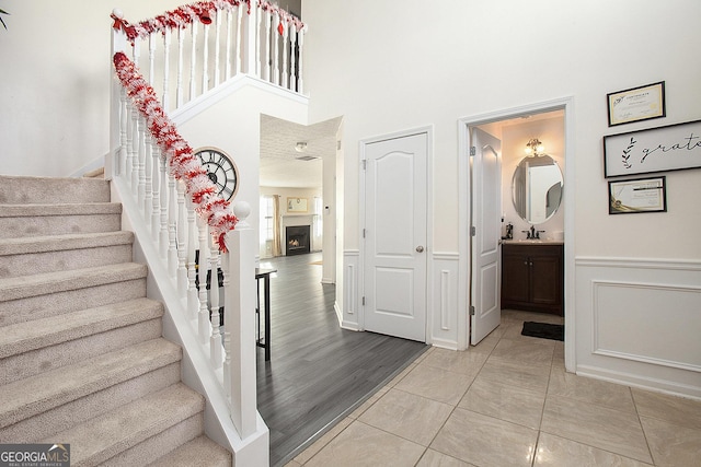 stairway featuring a decorative wall, a high ceiling, wood finished floors, a lit fireplace, and wainscoting