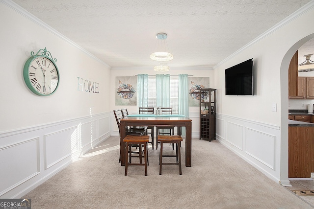 dining room featuring light carpet, arched walkways, ornamental molding, a textured ceiling, and a decorative wall